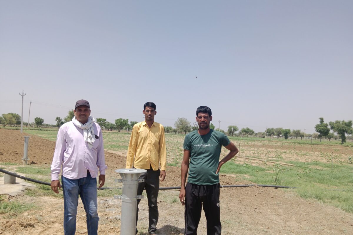 Manoj Kumar standing along with his brother Keshav Singh and friend Surajbhan Rayala, at Chainpura village in Jhunjhunu district. The pillar in the photograph was established when the solar panels were installed for the solar pump. As the groundwater level depleted, he sold the solar set up as the pump could not draw water anymore from those depths. Photo by Parul Kulshrestha/Mongabay.